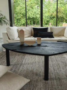 Table basse en bois brûlé à trois pied sur tapis en tissus de chez Mille & Claire